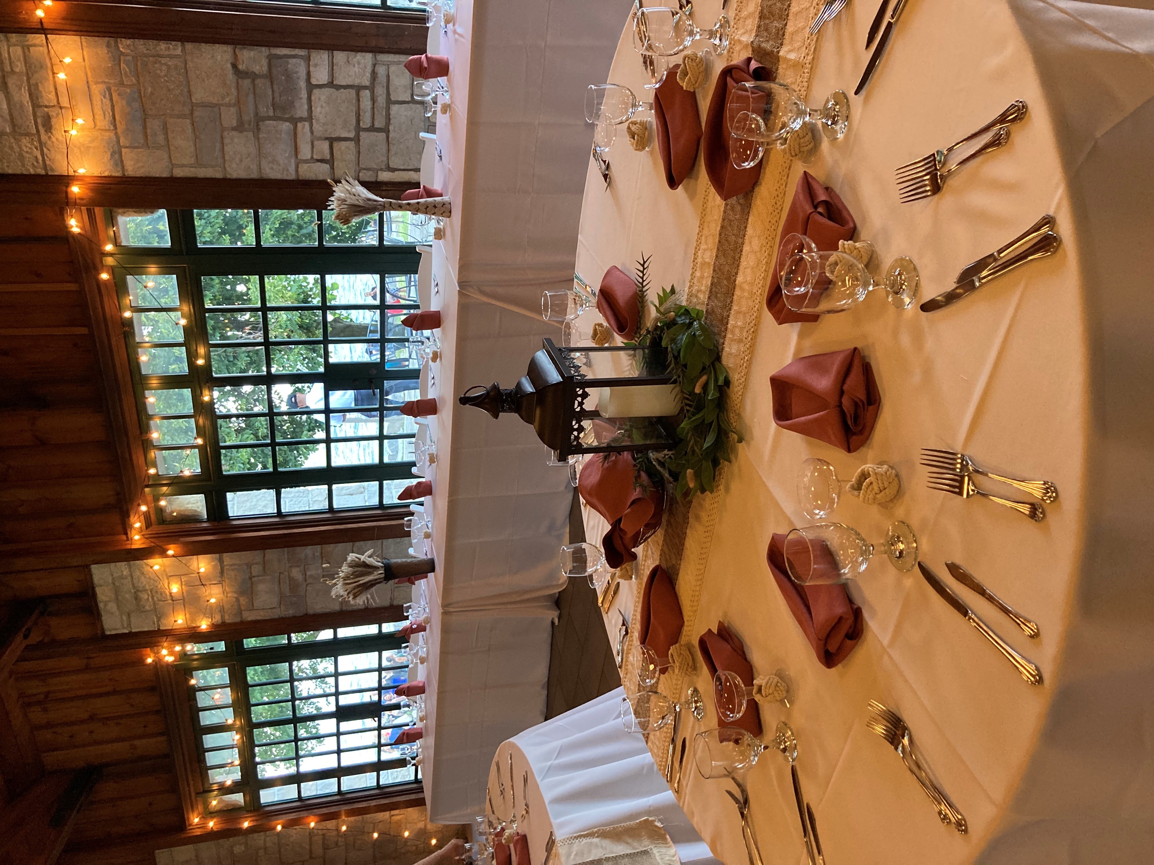 Wedding reception tables with rust-colored napkins and string lights by windows.